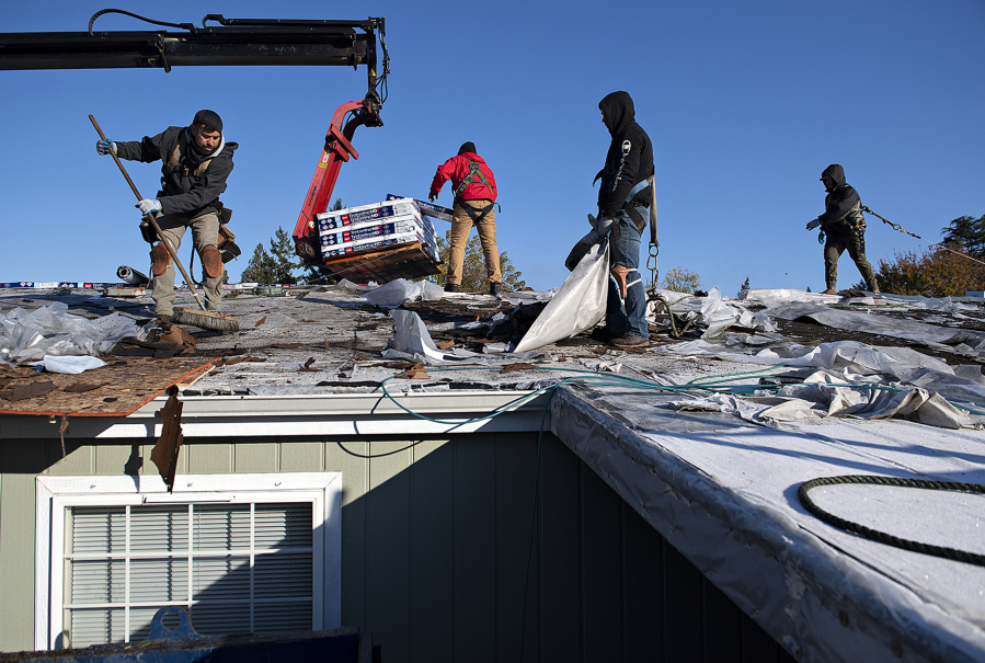 Matrix Roof and Home roofers Alfredo Mendoza, left, and Jorge Gutierrez, second from right, lend a hand as construction continues on the roof of a low-income senior, Lynn, on Wednesday morning. The roof repair enables Lynn to stay in her home after receiving a cease-and-desist notice in September demanding she repair her failed roof within five days.